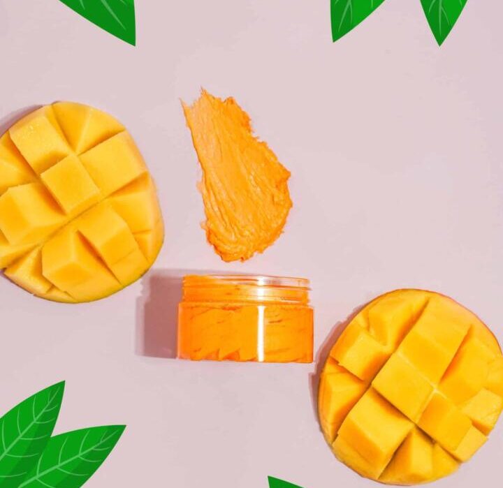 Mango slices and a jar of mango puree on a light pink background with green leaves.